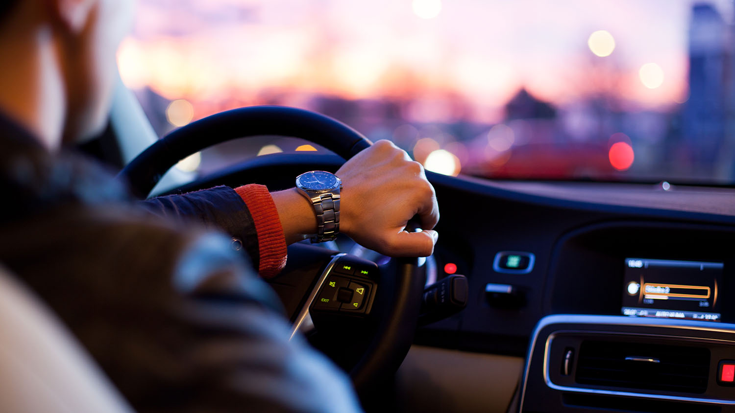 guy driving in the sunset with one hand on the steering wheel 