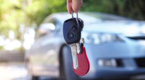 Someone holding a set of keys in front of a car.