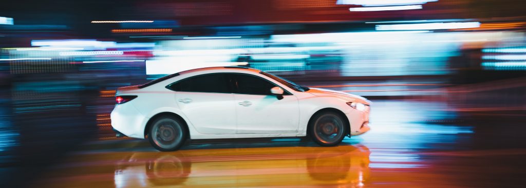 A white car with professional window tinting driving through the city at night.