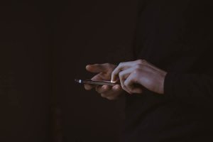 A person standing in the dark taps their smartphone.