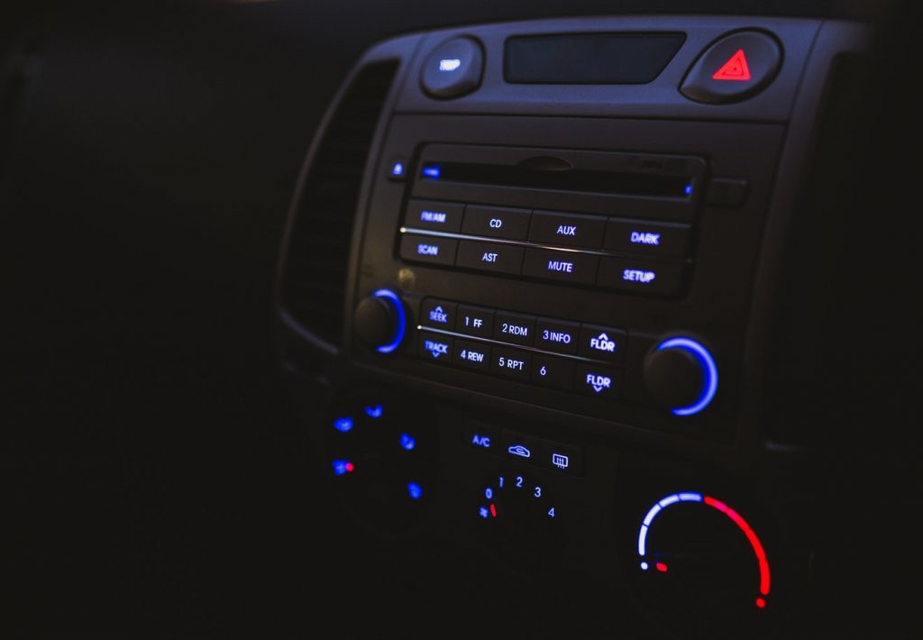 A car stereo system is gently lit by the glow of its own lights in a darkened car dashboard.