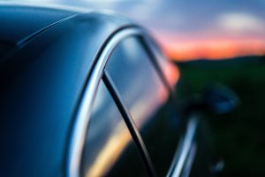 A dark car with tinted windows sits in the light of a glowing sunset.